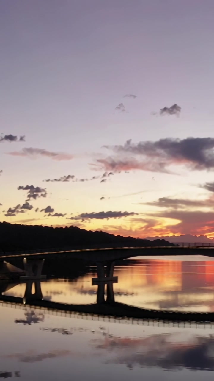 Vertical video: Camera panning arched bridge as sunset deepens at lake, showing vivid reflection