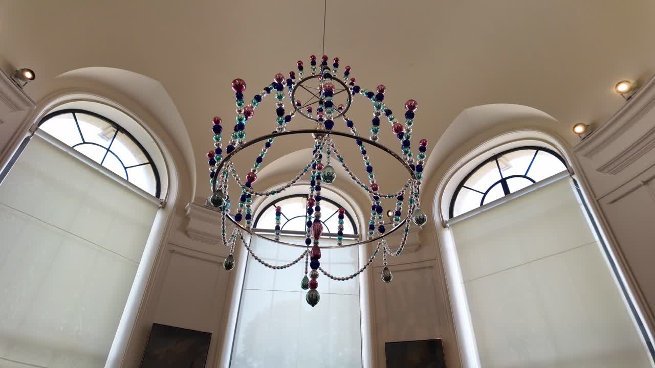 Chandelier adorned with colorful crystal beads, suspended in grand interior with arched windows and soft natural lighting, Low angle pov