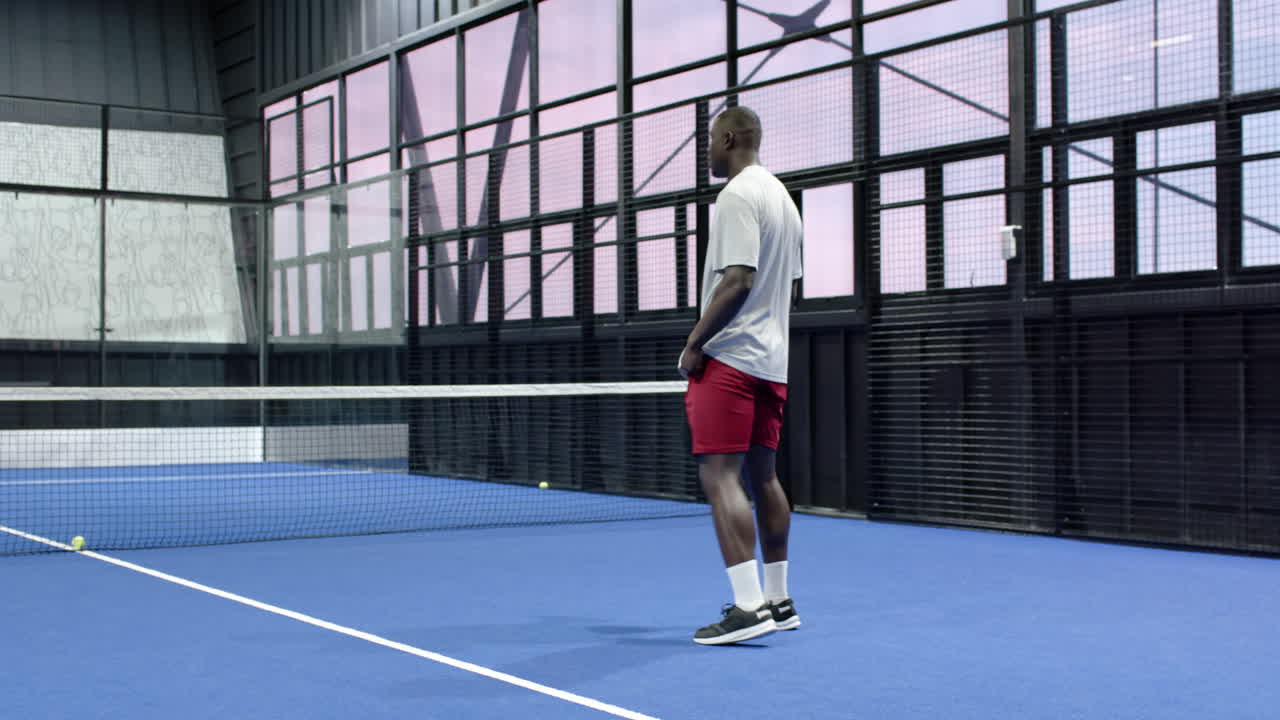 Man playing padel tennis on blue indoor court, preparing to hit ball with racket