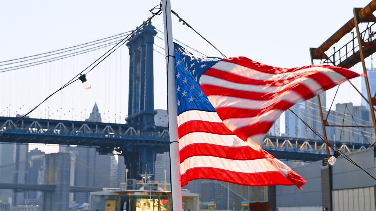 Albero della barca con bandiera americana che sventola al vento. Il Ponte di Manhattan con vista dal basso sullo sfondo