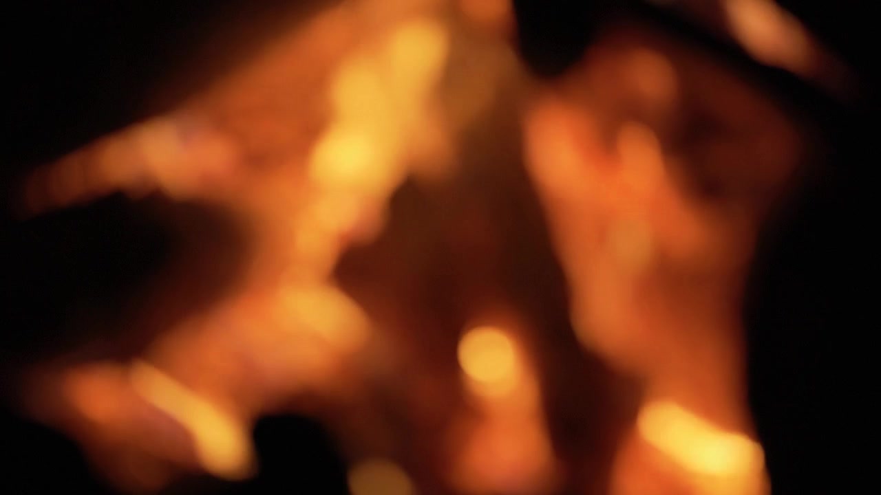 Abstract blurry bokeh background of warm orange campfire flames flickering softly in the pitch dark night with glowing light.
