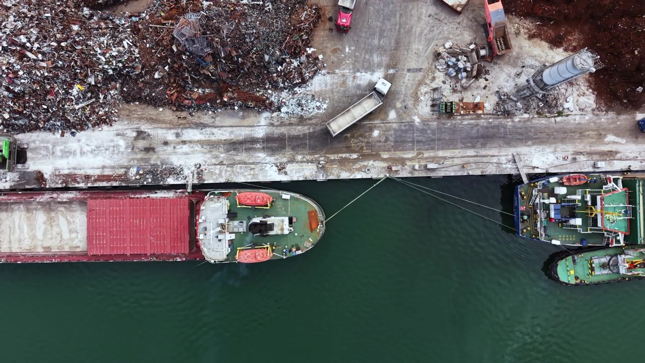 Buque de carga descarga en el puerto mientras maquinaria y escombros yacen en el muelle durante el día en una zona industrial.