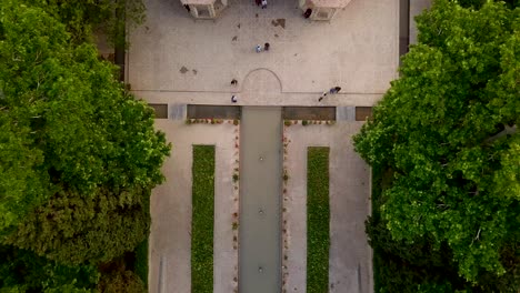 Aerial-moving-down-on-a-Persian-garden-with-a-beautiful-historical-palace-building,-green-trees-and-stream-in-yard-in-Kerman-Iran