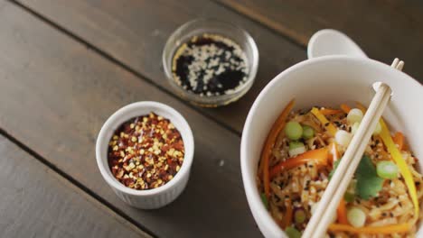 composition of bowl of pad thai with soy sauce and chopsticks on wooden background