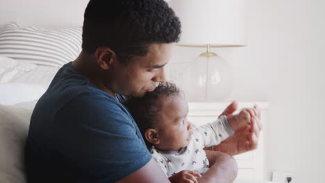 millennial african american dad rocking in an armchair holding his baby boy, close up, side view