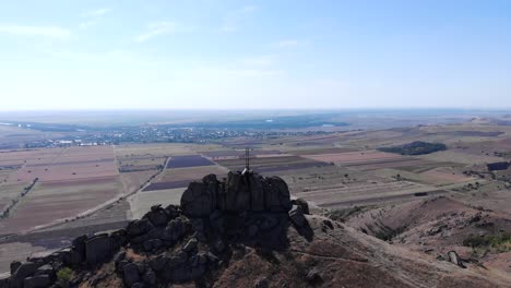 Vista-De-Una-Cruz-En-El-Pico-Pricopan-Con-Fondo-De-Tierras-De-Cultivo-En-Macin-Mountain,-Dobrogea,-Rumania