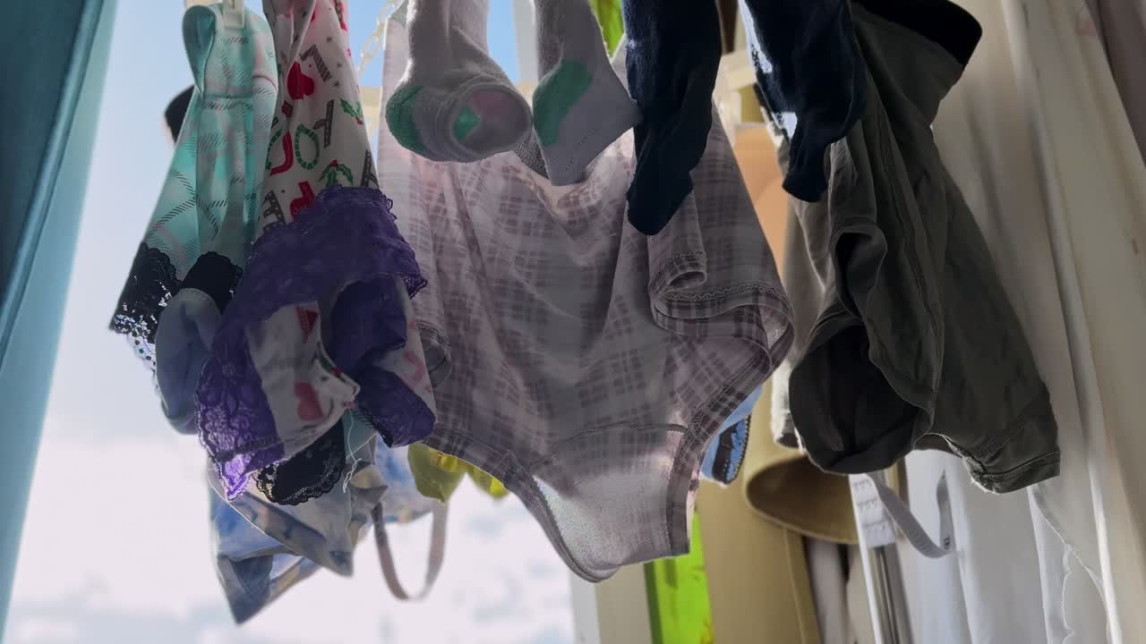 Low-angle view of freshly washed underwear and socks hanging to air dry by a sunlit apartment window, capturing an everyday indoor household laundry routine in natural daylight
