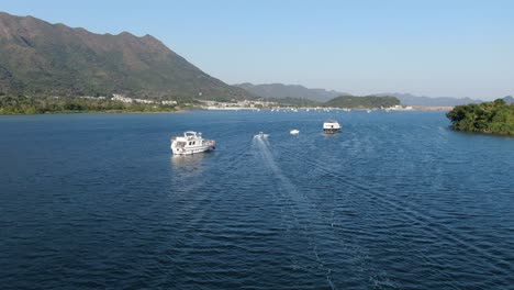 Hong-Kong-bay-with-small-boats-and-surrounding-green-landscape,-Low-pass-aerial-view