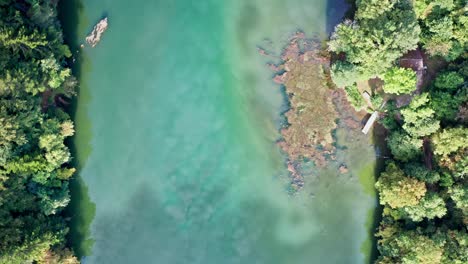 Clouds-reflected-in-deep-green-blue-water-of-river-through-forest,-aerial-drone