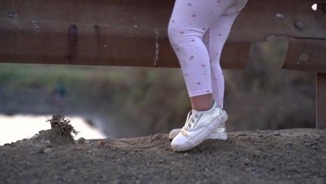 pequeña niña negra sudafricana parada en arena gris señalando el pie izquierdo