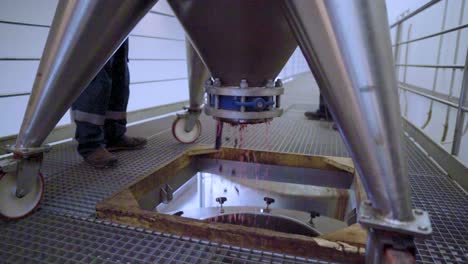 Crushed-grapes-falling-down-a-funnel-into-a-stainless-steel-tank,-wine-process