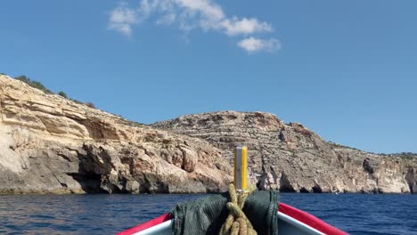 Traditional-luzzu-fishing-boat-swaying-in-mediterranean-sea-waves-next-to-Blue-Grotto-coastline-in-Malta-on-a-sunny-summer-day