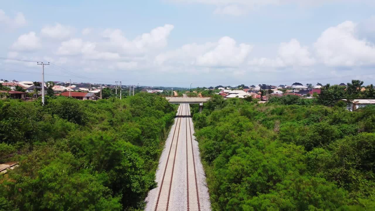 Beautiful aerial of long train tracks running through a peaceful landscape in rural Nigeria with the skyline of a small town in the background