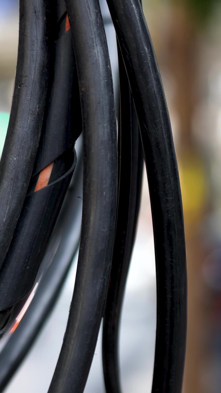 Macro shot of thick black utility wires hanging against a blurred urban background.
