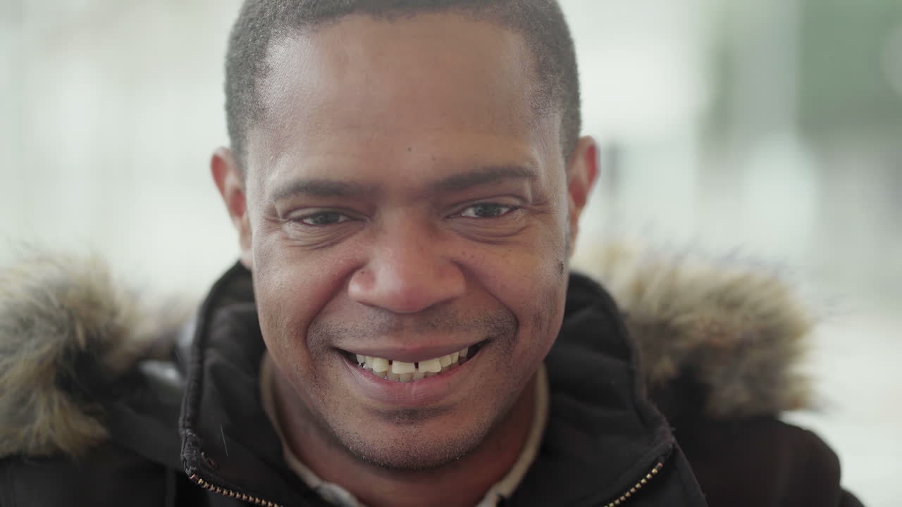 hombre afroamericano de mediana edad con chaqueta negra y capucha de piel sentado afuera