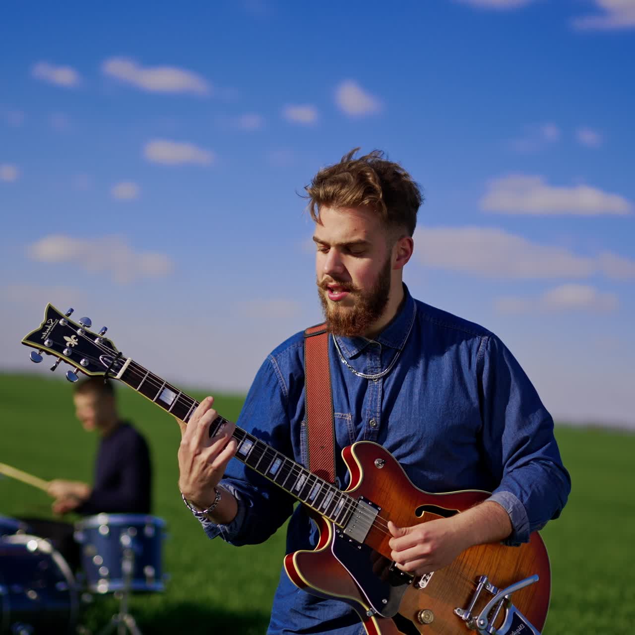 Caucasian bearded man playing guitar passionately and singing. Male drummer playing the drums on the drum kit at backdrop in blur