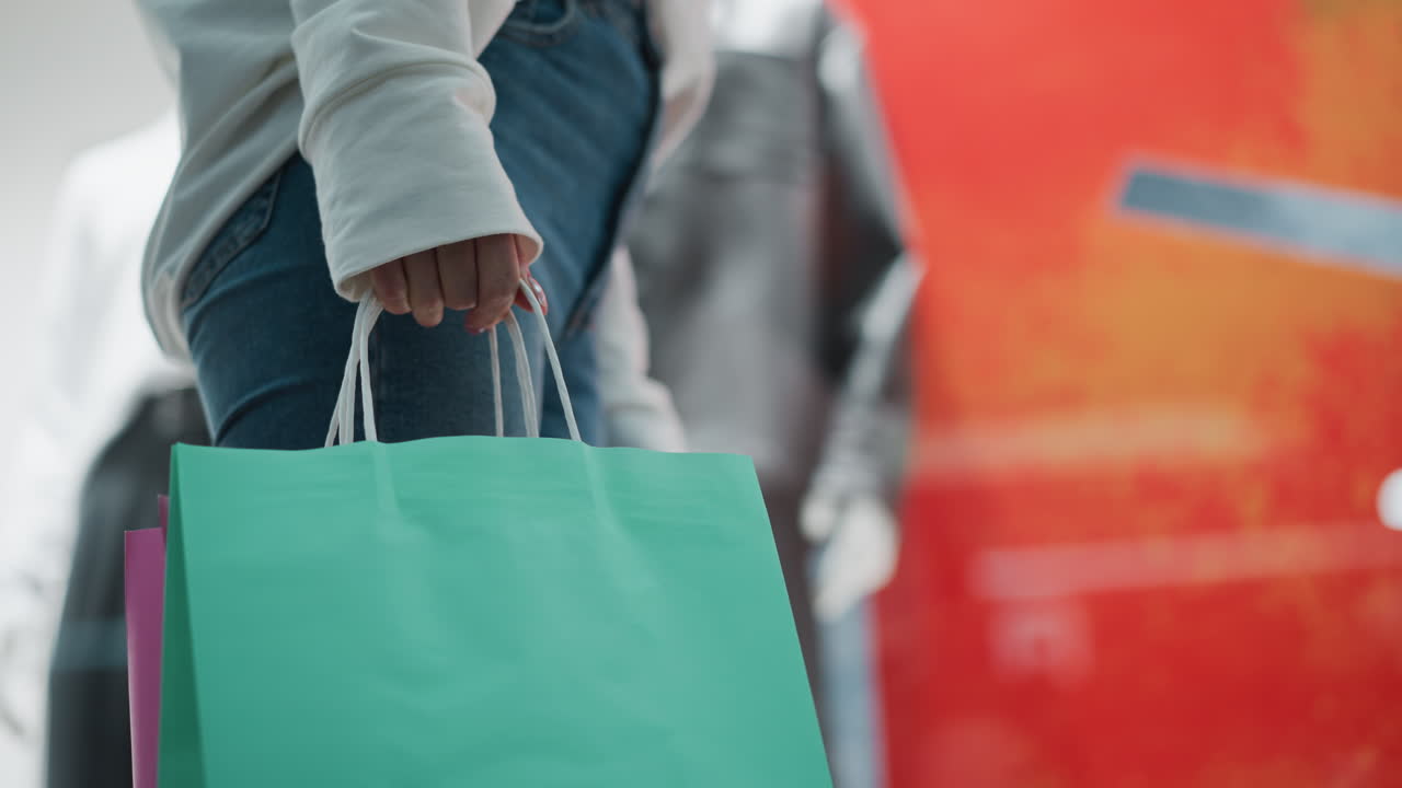 멘트 쇼핑 가방을 들고 서 있는 여성의 측면 시각 부드럽게 흔들리고, 캐주얼한 색 부분과 청바지를 입고, 흐릿한 마네킨과 활기찬 빨간색 배경을 가지고 있습니다.