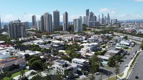 Flying-over-small-hotels-in-Australia,-skyscrapers-and-the-ocean-on-the-background