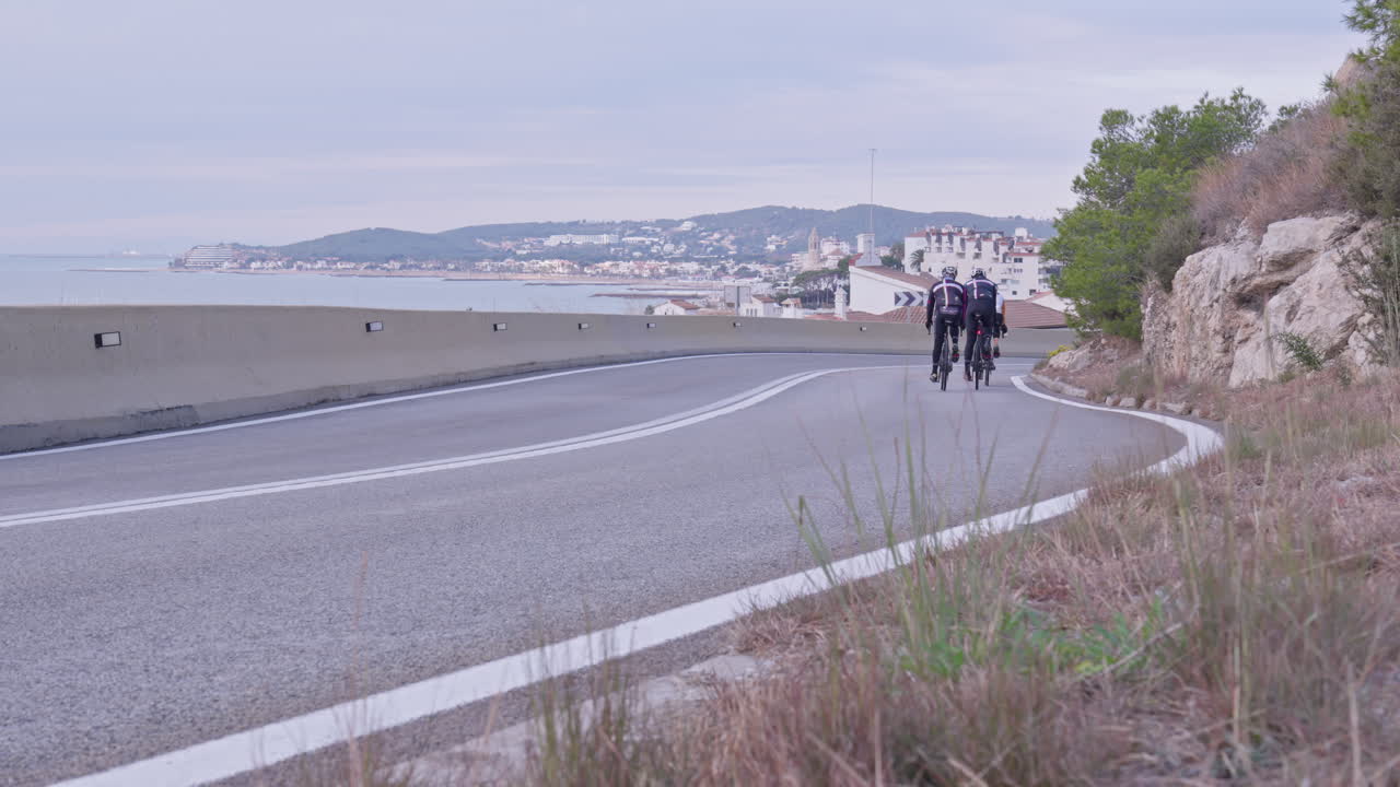 한 무리의 자전거 타는 사람들이 그림 같은 해안 도시를 향해 구불구불한 길을 질주합니다.