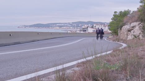 a pack of bicyclists speed down a winding road as they make their way towards the picturesque coastal city