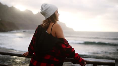 Woman-gazes-at-ocean---A-brunette-woman-shown-from-behind-looks-out-over-an-ocean-in-front-of-the-hills,-and-then-turns-and-walk-away.-Cloudy-weather.-Slow-motion