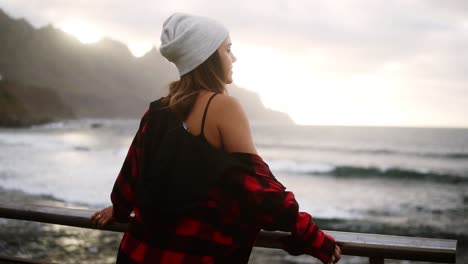 woman gazes at ocean - a brunette woman shown from behind looks out over an ocean in front of the hills, and then turns and walk away. cloudy weather. slow motion