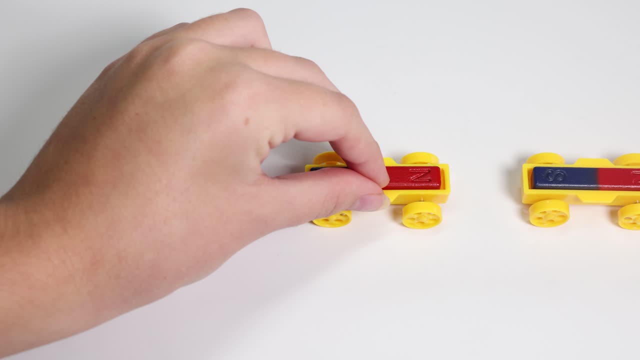 Hands manipulate magnetic toy cars on a white surface, illustrating magnetic attraction and repulsion in a well-lit environment