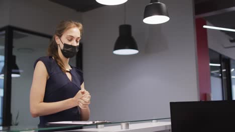 caucasian woman in face mask disinfects hands and signs in at office reception desk