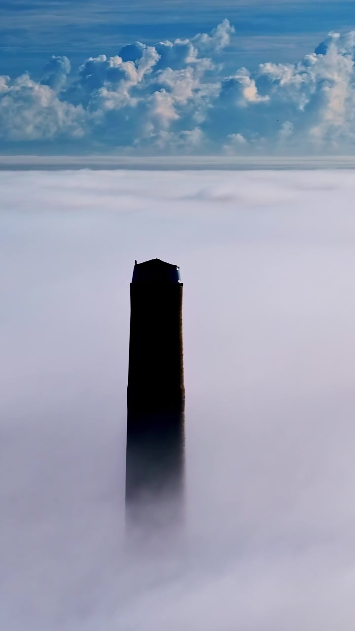 Silhueta mística de torre escura emergindo de um denso mar de neblina sob um céu azul com nuvens.
