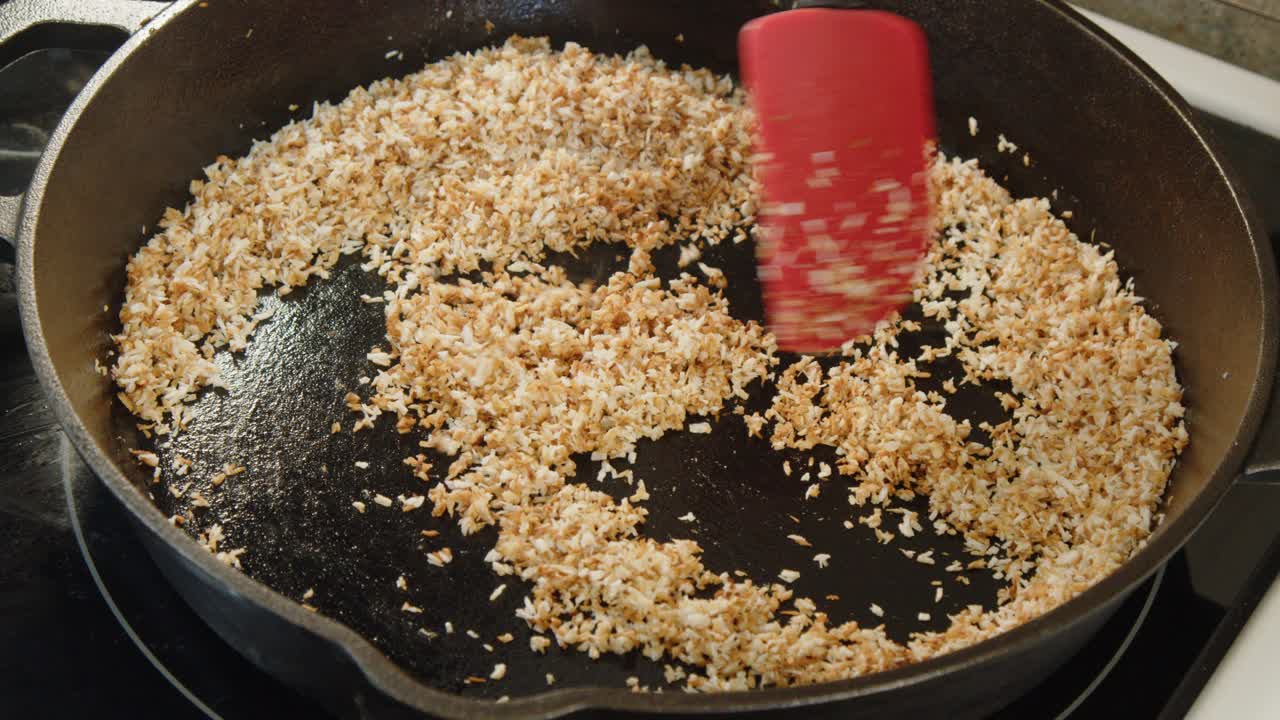 Kookosraaste paahdetaan kullanruskeaksi lähikuvassa valurautapannussa.
