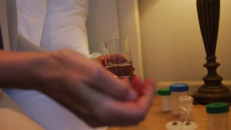 ältere kaukasische frau sitzt im schlafzimmer und nimmt tabletten mit einem glas wasser