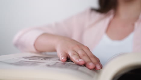 woman strokes photo album page indoors closeup. lady studies family history looking at relatives pictures in book. remembering past times and youth