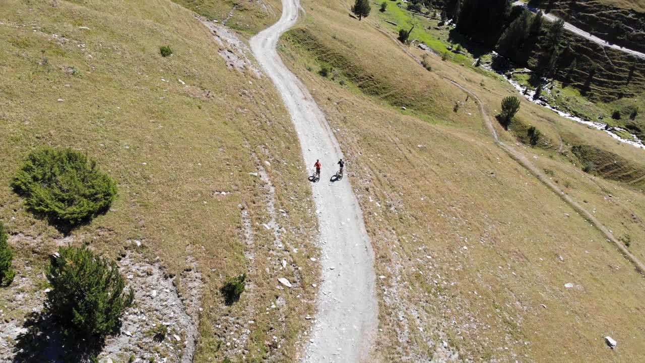antena: dos ciclistas de montaña que van cuesta abajo en una alta montaña en verano