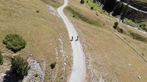 aerial: two mountain bikers going downhill in a high mountain in summer time