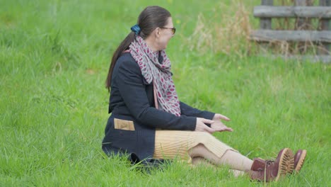 A-middle-aged-woman-sits-on-the-grass-and-plays-with-a-small-white-dog