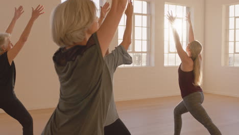 clase de yoga de mujeres maduras sanas que practican pose guerrera disfrutando del ejercicio físico matutino en el estudio al amanecer.