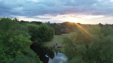 Aerial-footage,-slowly-descending-at-sunrise-looking-out-across-the-Stour-valley-to-the-river-stour-with-a-woman-gently-paddle-boarding-towards-the-camera-in-summer