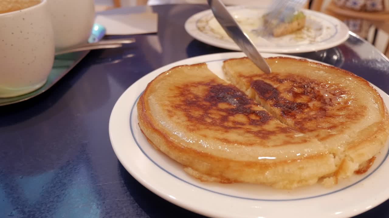 Fluffy pancake on a plate being cut with a knife and fork in a cozy setting
