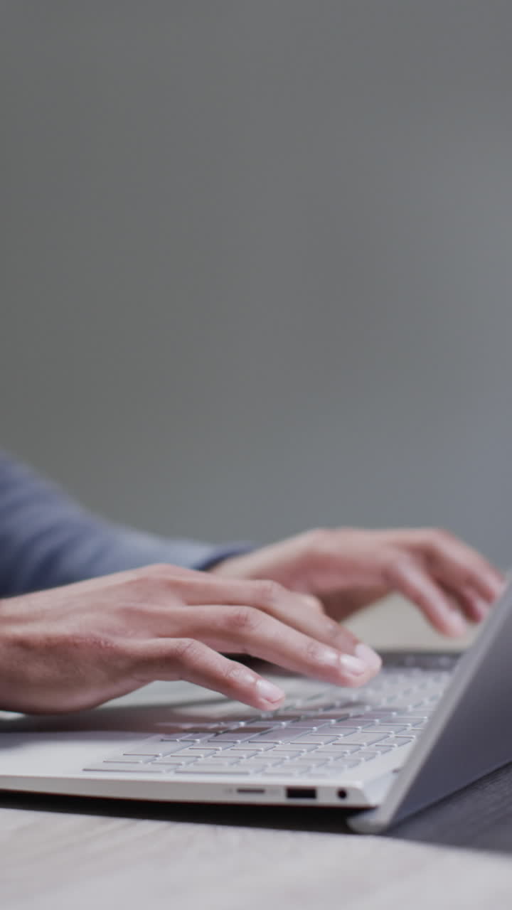 Vertical video of biracial businessman using laptop on grey background