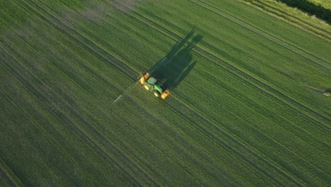 Vista-Aérea-De-Establecimiento-De-Un-Agricultor-Rociando-Campos-De-Cultivo-Con-Tractor,-Rociando-Pesticidas-Y-Fertilizantes,-Tarde-Soleada-De-Verano,-Luz-De-La-Hora-Dorada,-Tiro-Amplio-De-Drones-De-Ojo-De-Pájaro-Moviéndose-A-La-Derecha