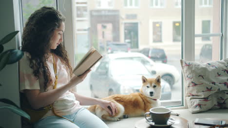 woman reading a book with dog by the window