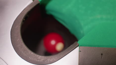 close-up upshot captures red billiard ball rolling smoothly into pool table pocket on green surface. motion blur emphasizes movement, precision, and strategy, highlighting accuracy, competitive