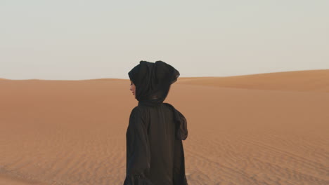 retrato de una hermosa mujer musulmana con hiyab caminando en un desierto ventoso y mirando a la cámara