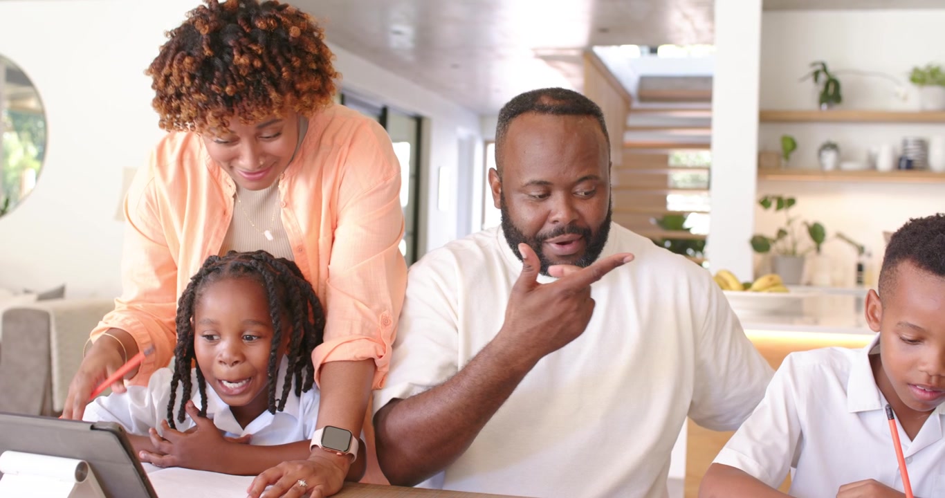 Famiglia afroamericana: la mamma esorta la figlia a leggere con il tablet per i compiti mentre il padre guida il figlio.