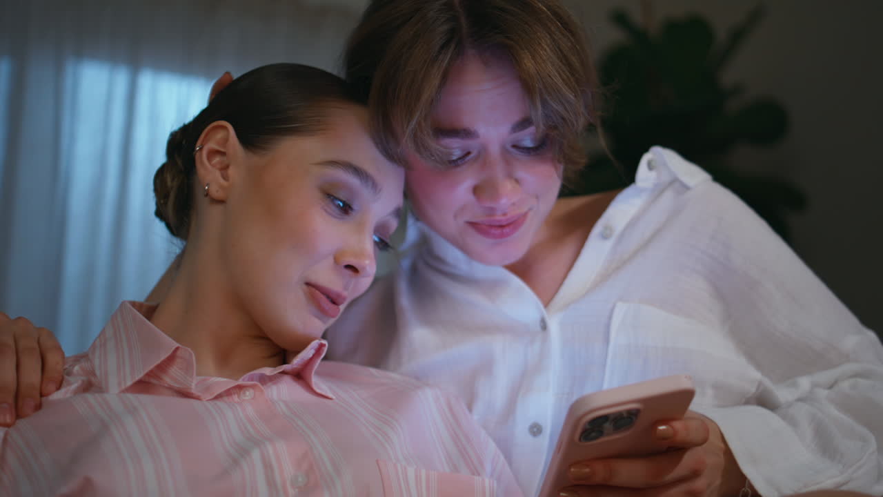 Woman supporting sad friend reading bad news in smartphone at night home closeup