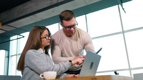 man and woman discussing work issues. male is asking questions and female is pointing at her laptop screen.