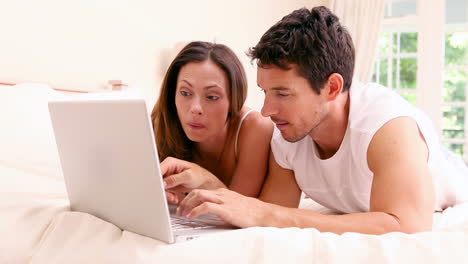 pareja feliz acostada en la cama usando una computadora portátil juntos
