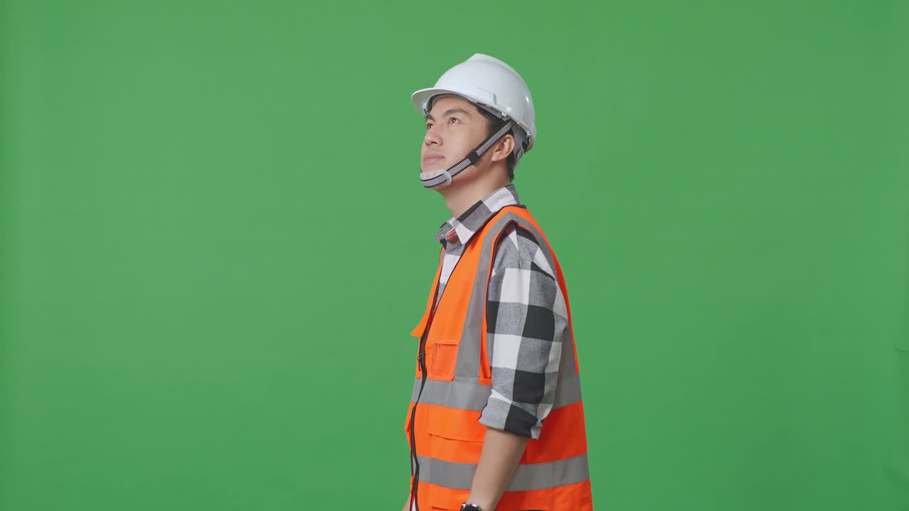 Side View Of Asian Male Engineer With Safety Helmet Looking Around While Standing In The Green Screen Background Studio