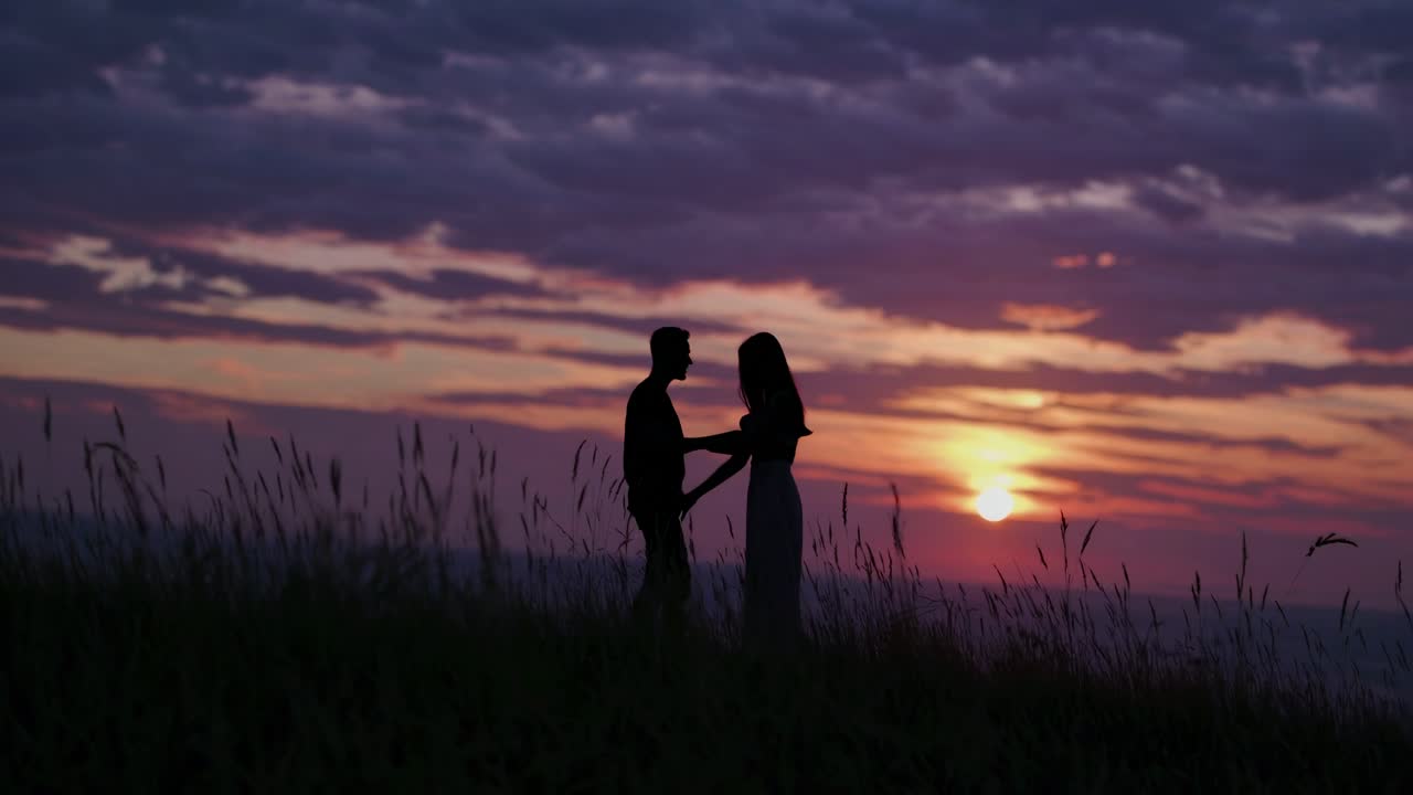 Silhouetted couple holding hands at sunset, captured from a low angle