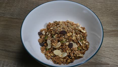 Acercar-Un-Tazón-Con-Granola-En-La-Mesa,-Nueces,-Pasas,-Semillas,-Frutos-Secos,-Desayuno-Saludable